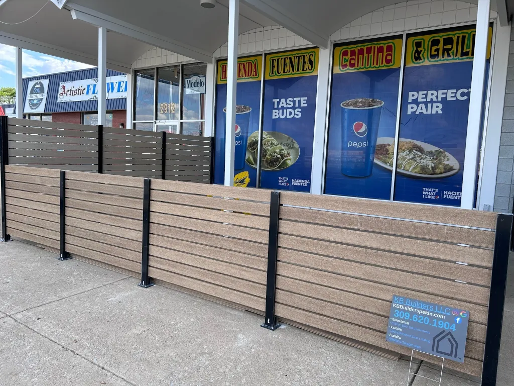 New brown and gray composite horizontal slat fencing for a restaurant patio with a sign for KB Builders LLC Top-Rated Construction Serving East Peoria, IL .