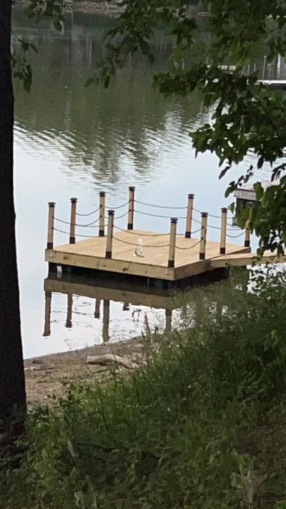 Newly built wooden dock with posts and chains on a calm body of water.