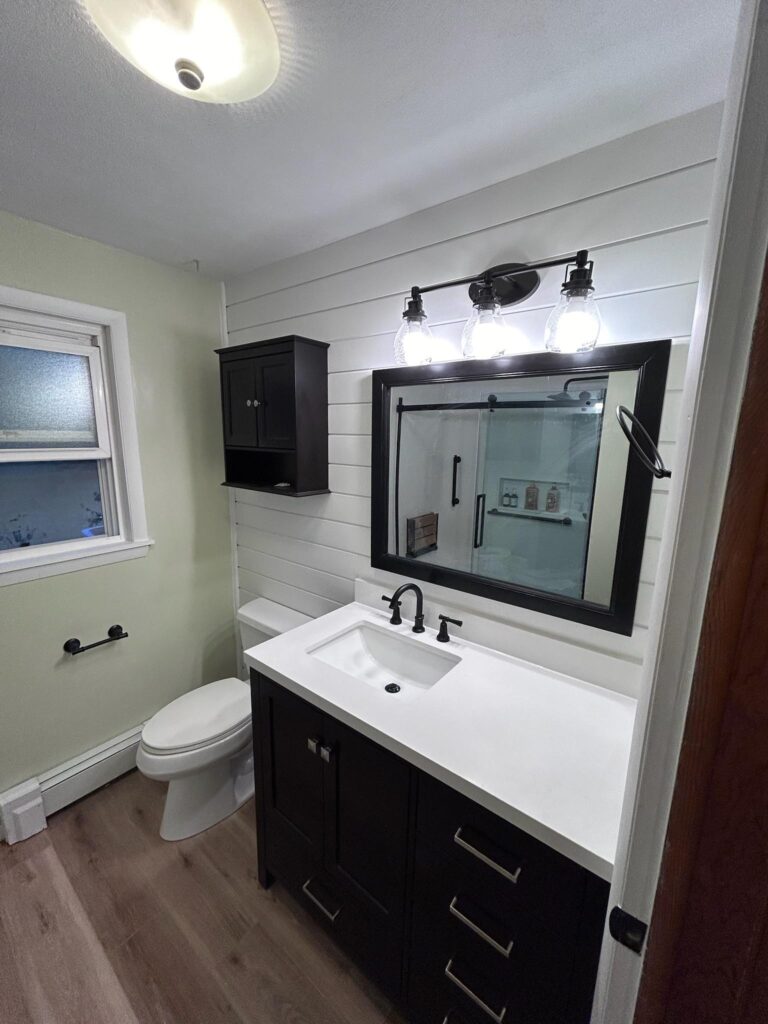 Modern bathroom with dark vanity, white shiplap wall, and large framed mirror.