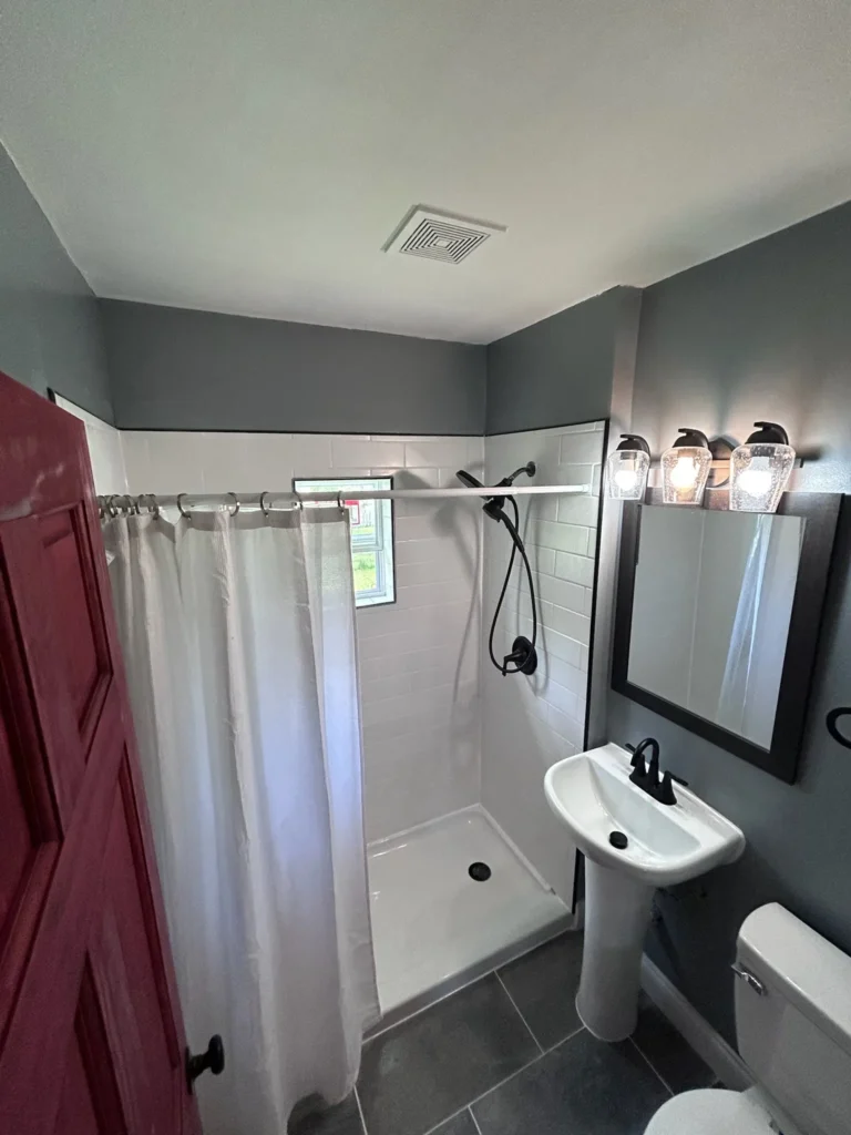 Compact bathroom with a white shower curtain, pedestal sink, and gray walls.