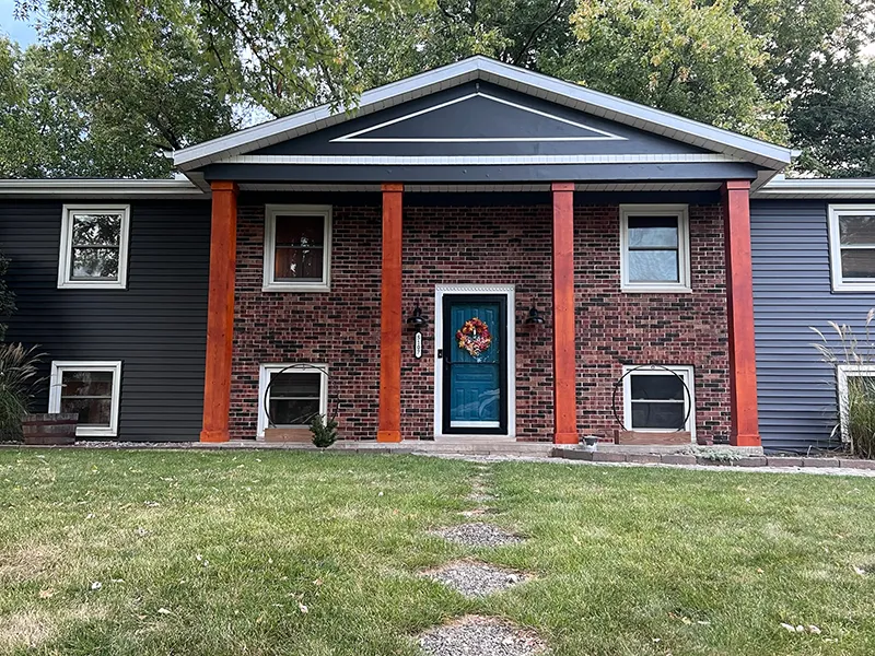 House with bold orange pillars, dark gray siding, and a blue front door with a wreath.