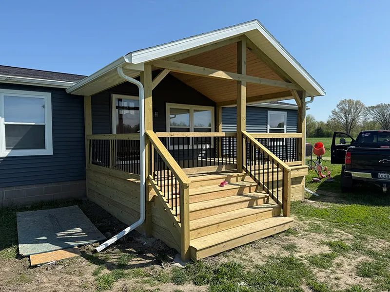 Newly constructed wooden porch with a gabled roof and dark blue siding on a house.