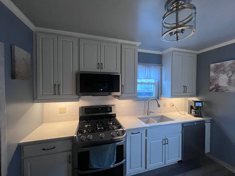 Modern kitchen with light gray cabinets, white countertops, a gas range, and under-cabinet lighting.