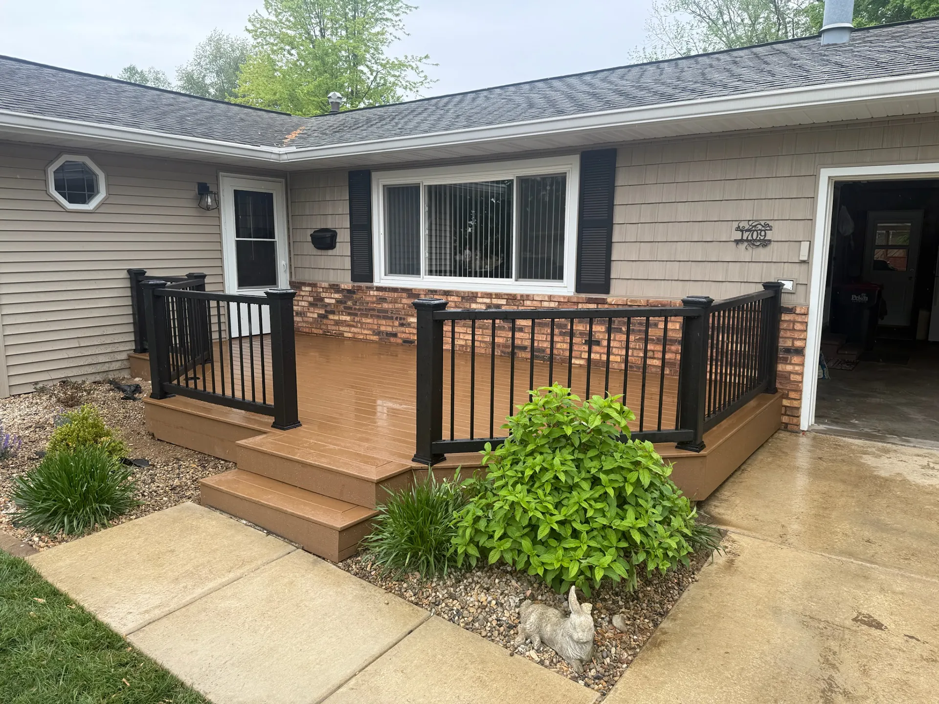 The front of a house featuring light brown horizontal siding, a brick accent wall, and a newly installed brown composite deck.