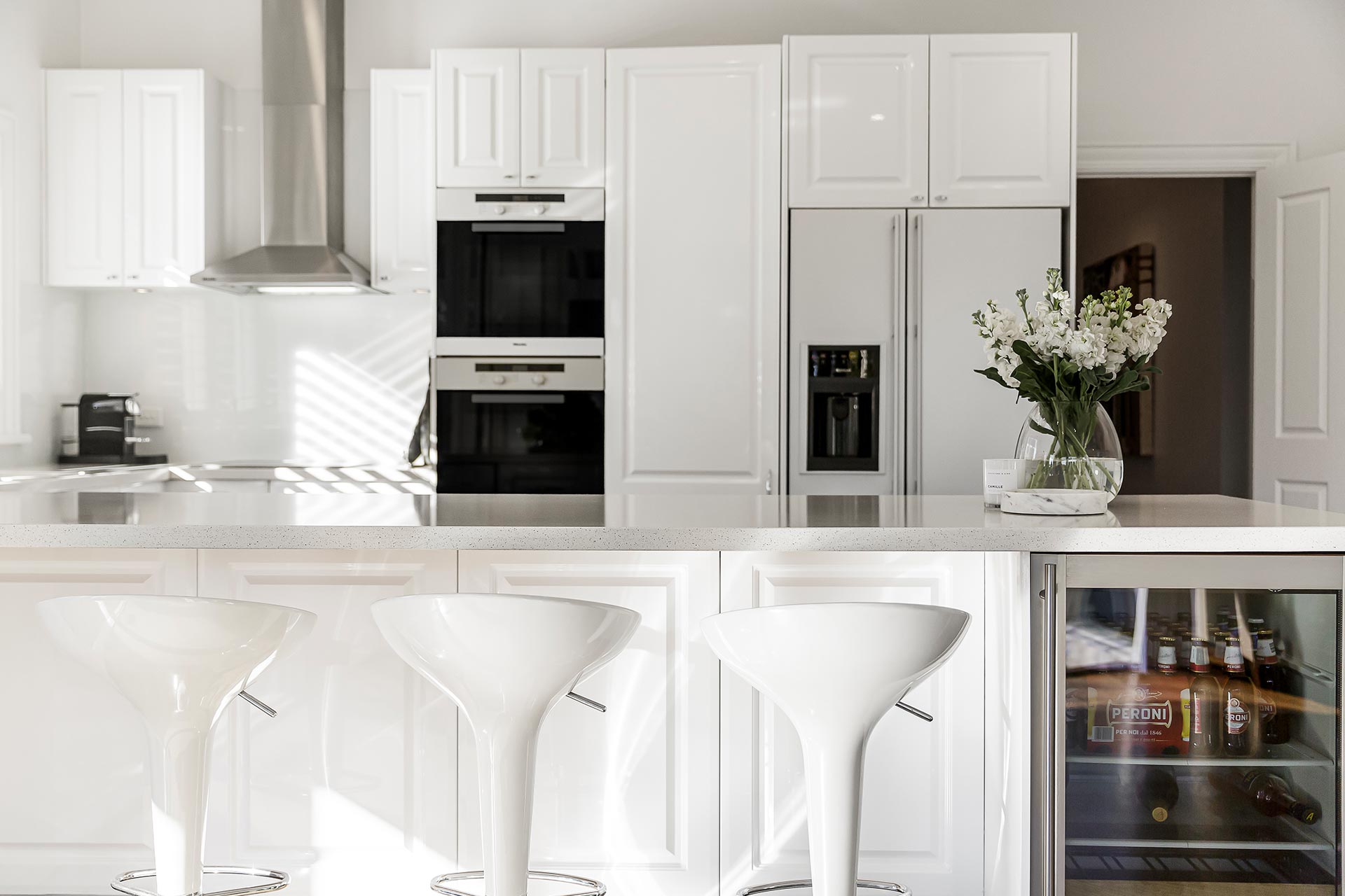 Canton, IL Best Construction Modern white kitchen with integrated appliances, island with white bar stools, and a beverage fridge