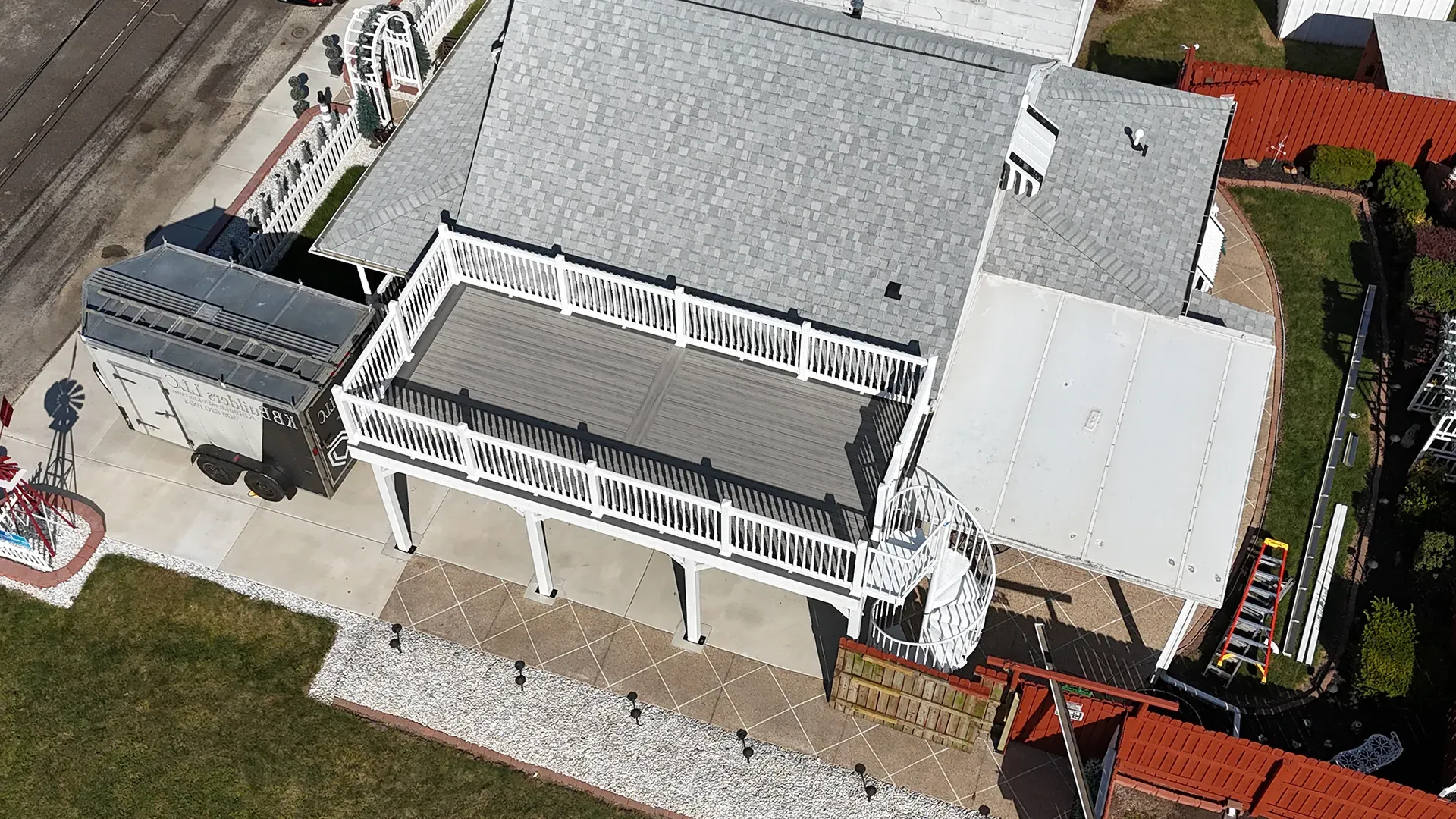 An aerial view of a two-story house with a newly constructed white deck featuring grey composite decking.