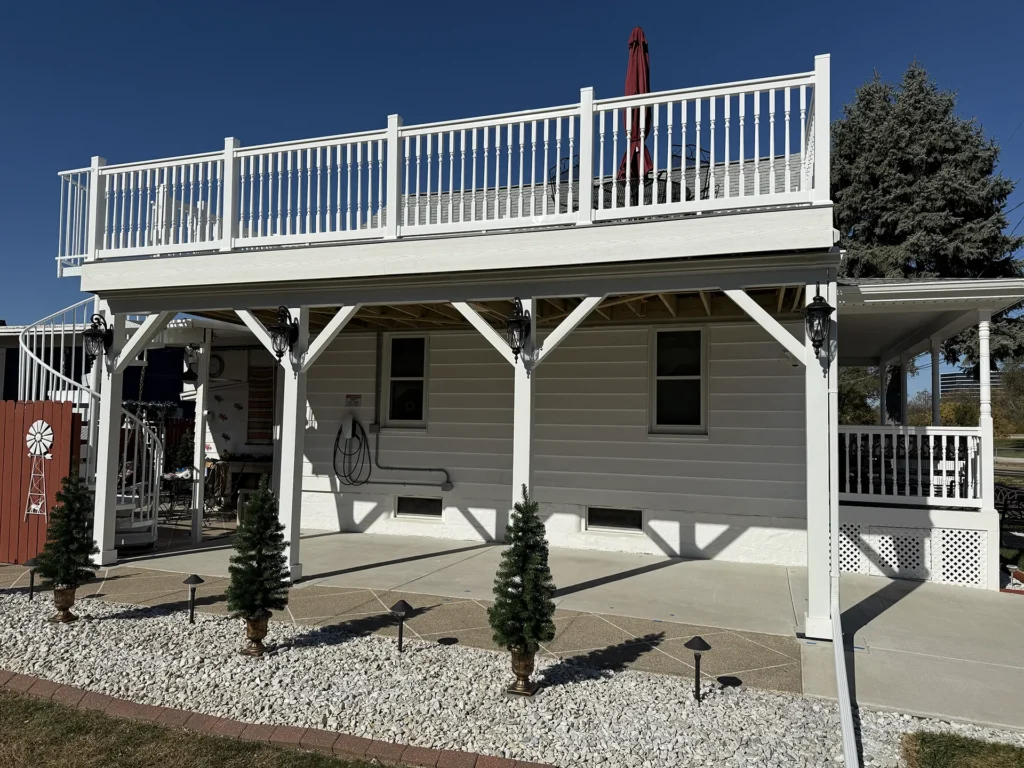 A two-story white deck with classic white balusters and a spiral staircase on the left side, extending from a white-sided house Top Construction Serving Creve Coeur, IL.