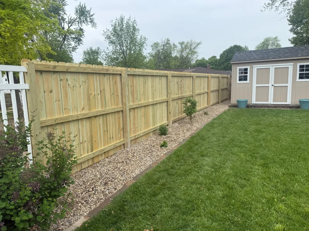 A long, newly installed wooden privacy fence with vertical pickets runs along the edge of a well-maintained backyard.