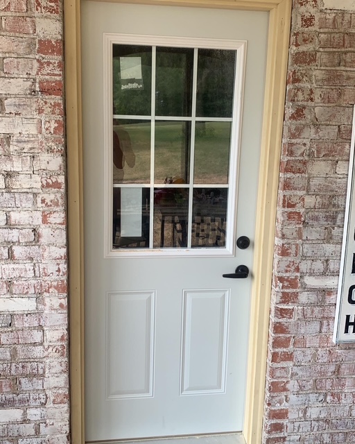 Close-up of a newly installed white exterior door with glass panes in a brick facade.