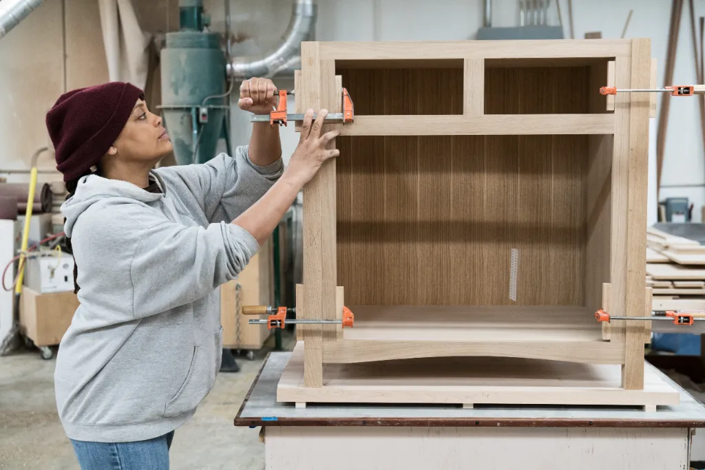 A custom cabinetry carpenter places clamps on her build.