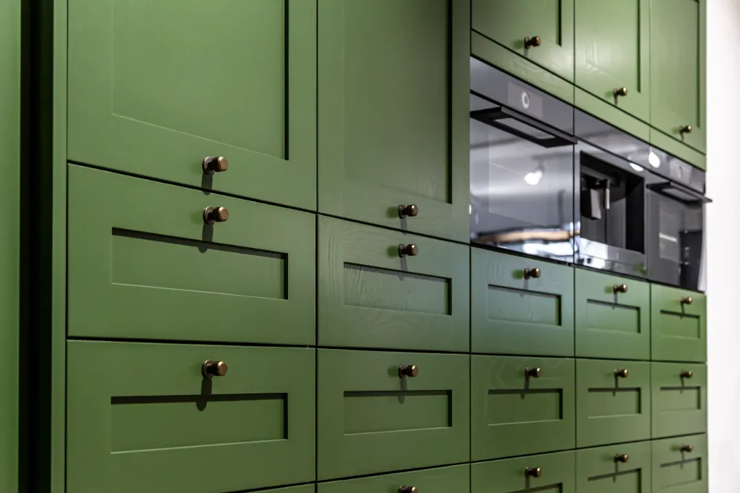 Closeup on a wall full of green kitchen cabinets built around an oven.