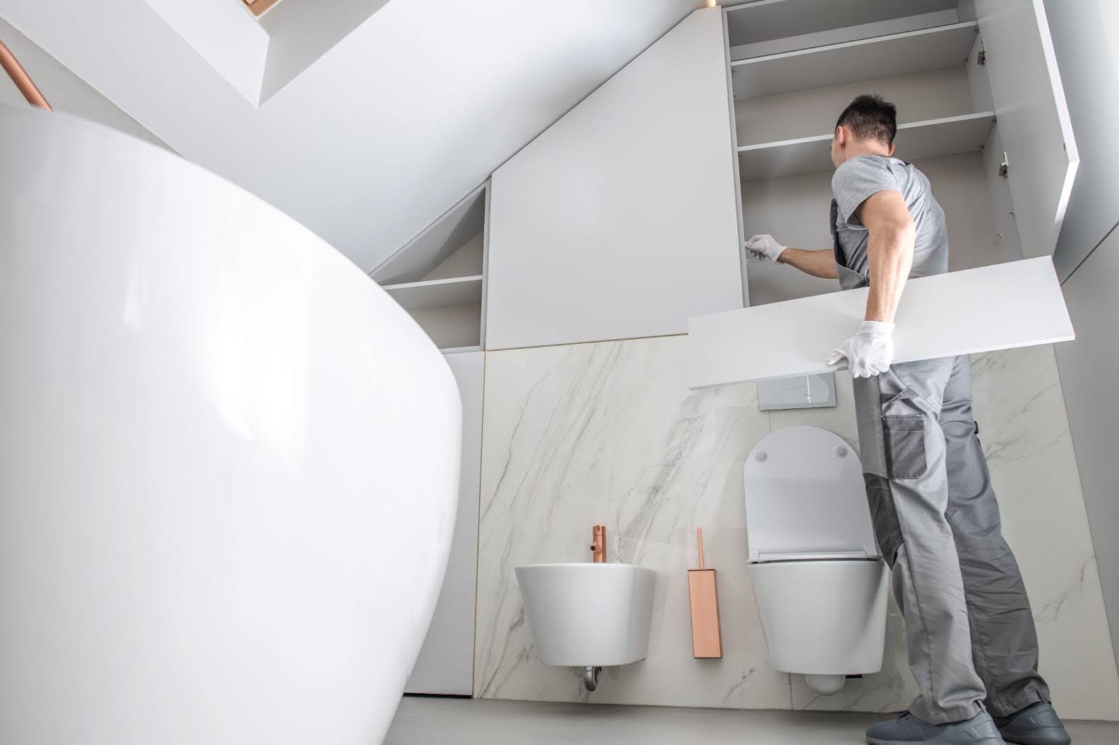 A construction worker is remodeling a white bathroom.