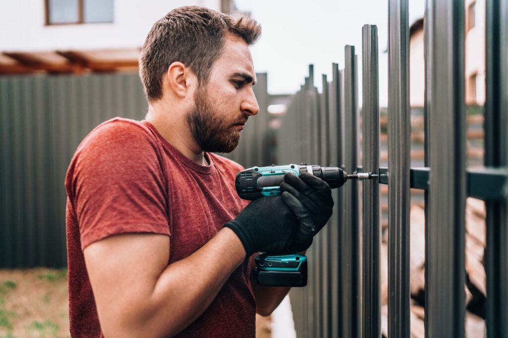 Skilled worker from a fence company fastening metal fencing components with an electric screwdriver during installation,
