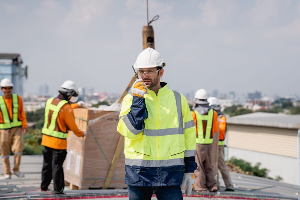 A contractor uses a radio to follow up on supplies as workers unload a delivery behind him.