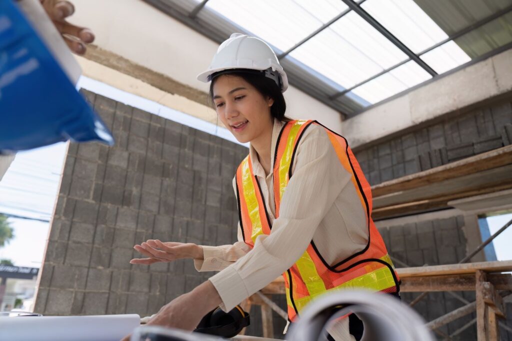 Asian female contractor reviews the construction plans on-site while managing project tasks.