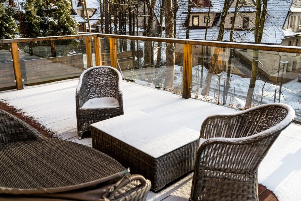  Snow-covered wooden deck featuring wicker chairs and a matching outdoor table.