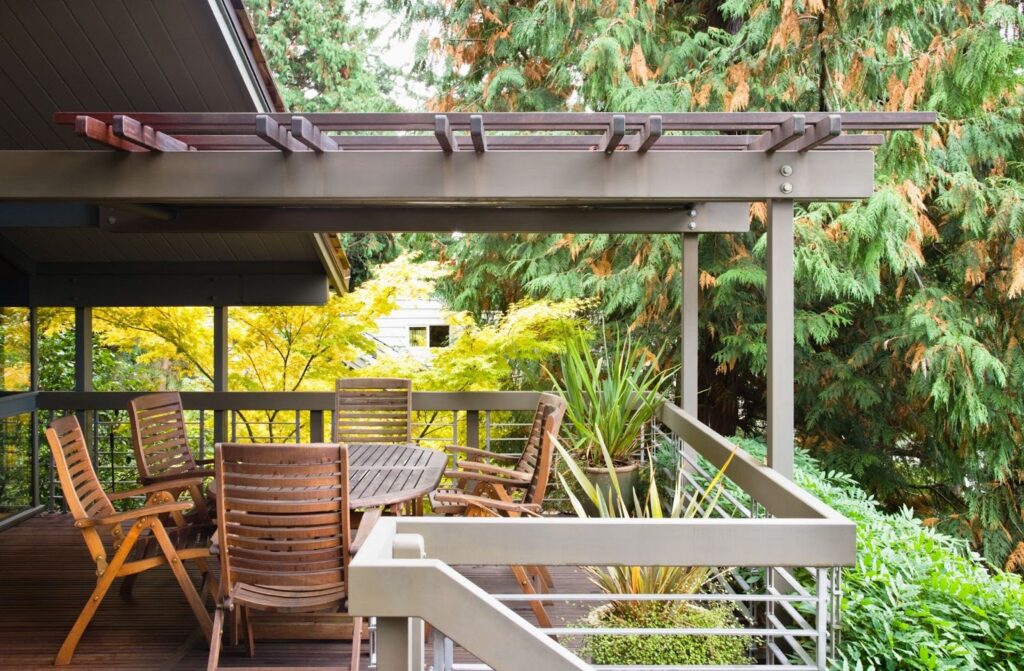 A compact covered wooden deck with matching wood furniture overlooking a lush green garden, designed for relaxing and seamless outdoor living.