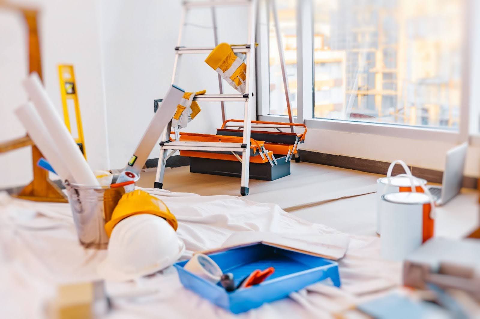 Interior workspace with construction tools, rolled blueprints, hard hats, a ladder, and paint supplies for home renovations.