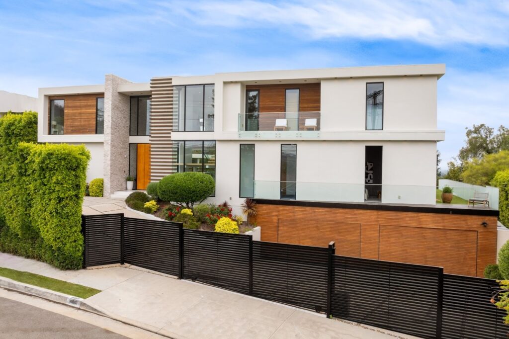 Contemporary corner-lot home surrounded by lush landscaping and a sleek black metal fence with horizontal slats