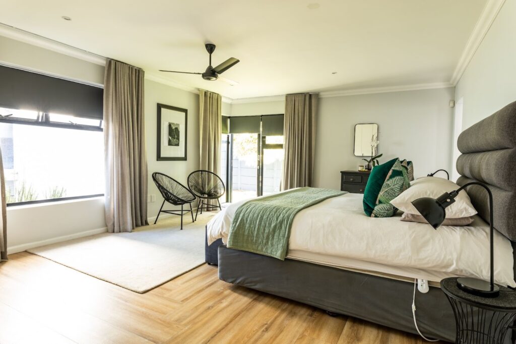Modern bedroom interior with large glass windows, green custom upholstered headboard, neutral furniture, and natural light