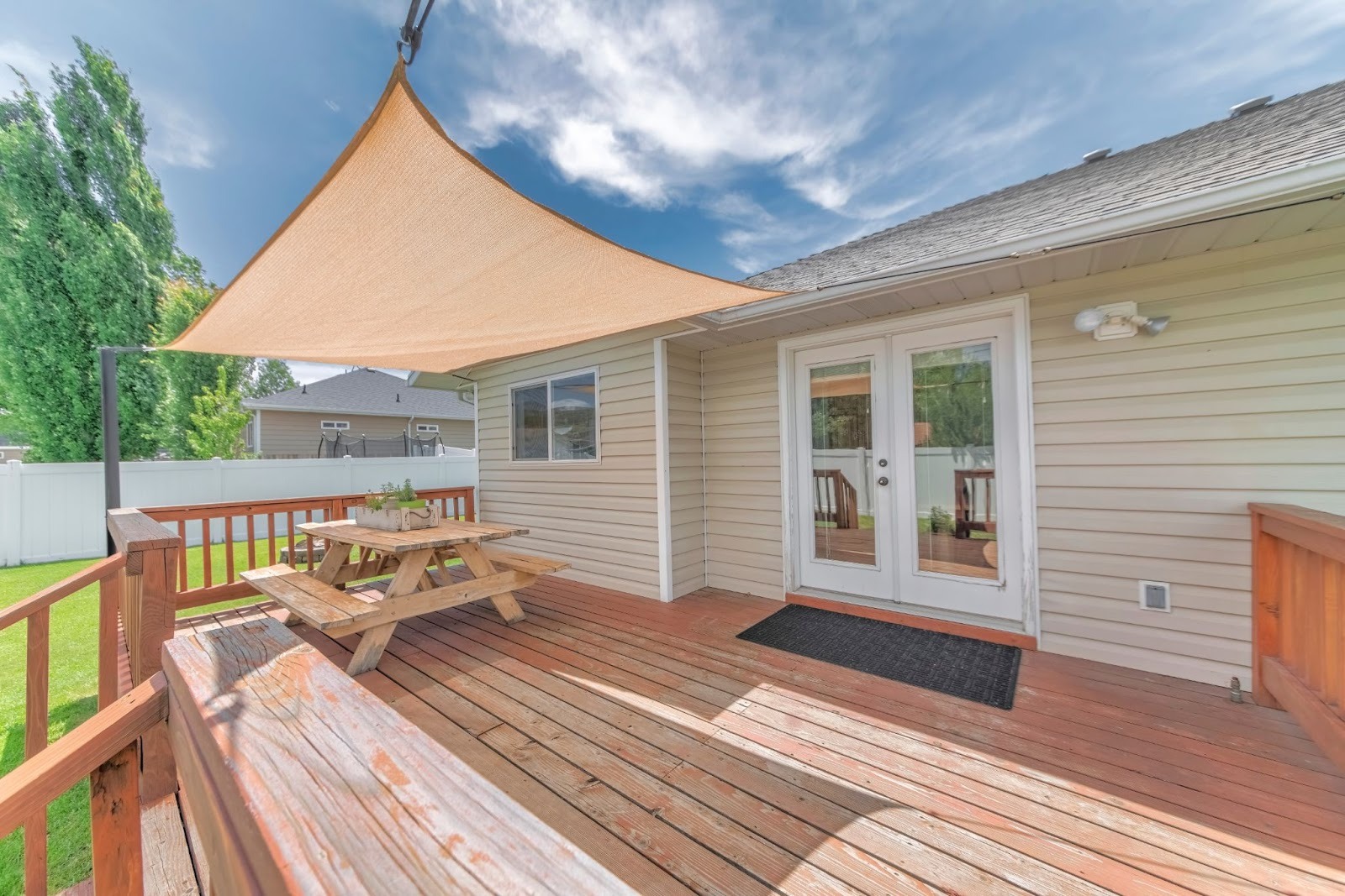 Private home wooden deck with outdoor seating and a dining table covered by a fabric sunshade canopy