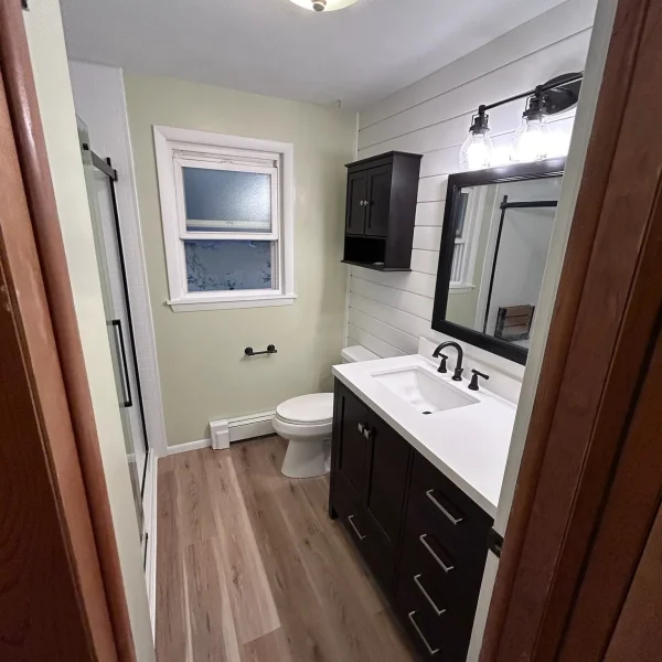 Renovated bathroom with dark wood vanity, white countertop, shiplap accent wall, and wood-look flooring