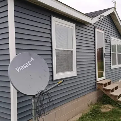 Side view of a house with gray horizontal siding, white windows, and a satellite dish.