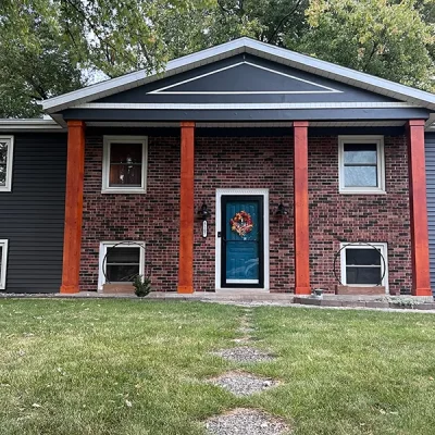 House with bold orange pillars, dark gray siding, and a blue front door with a wreath.
