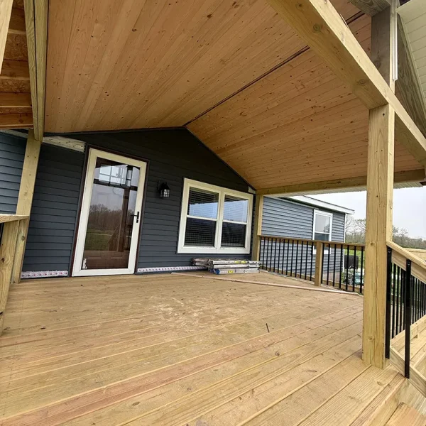 New outdoor deck with a light wood ceiling, dark siding, and a glass door.