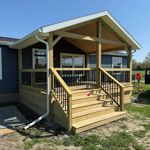 Newly constructed wooden porch with a gabled roof and dark blue siding on a house.