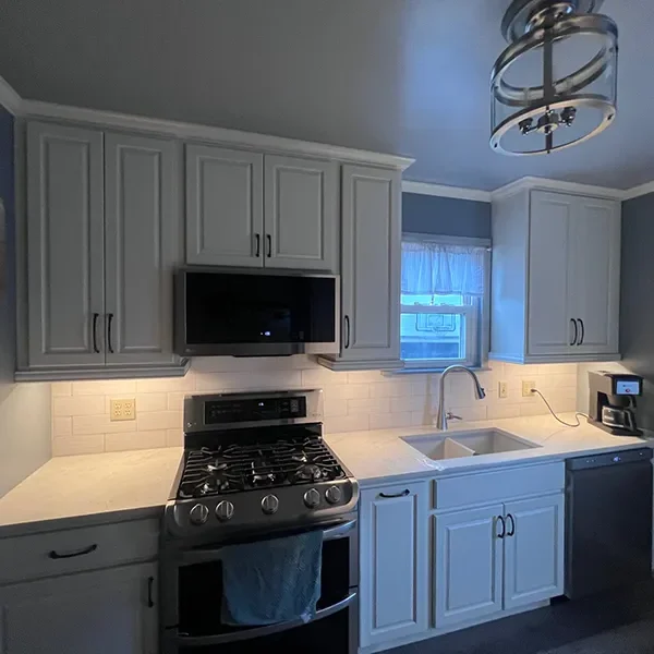 Modern kitchen with light gray cabinets, white countertops, a gas range, and under-cabinet lighting.