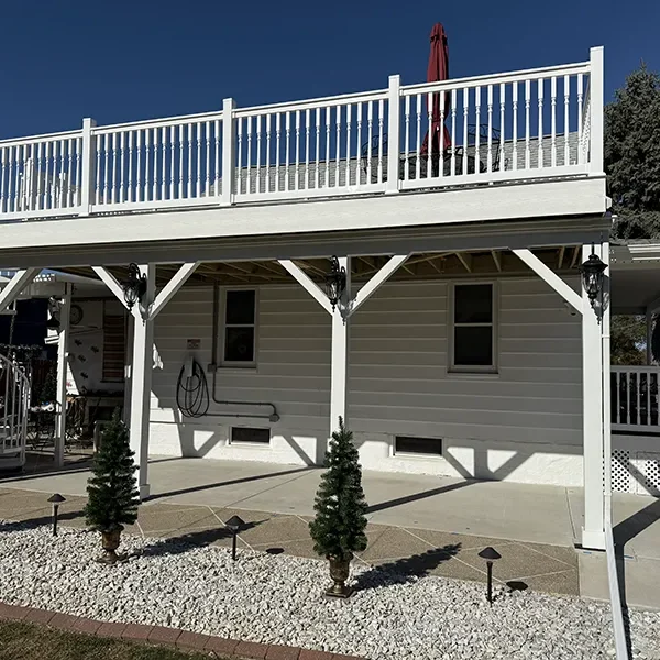 White elevated deck with a ground-level patio and decorative small evergreen trees.