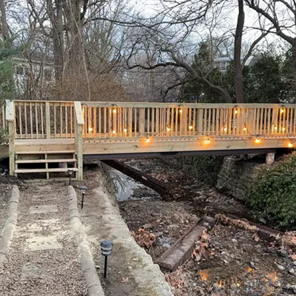 Elevated wooden deck with string lights, overlooking a sloped backyard and trees.