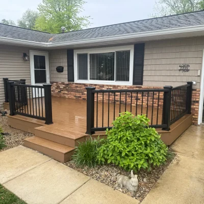 The front of a house featuring light brown horizontal siding, a brick accent wall, and a newly installed brown composite deck.