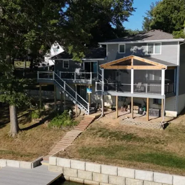 A gray waterfront lake house with a multi-level deck, a screened-in porch, and a staircase leading down to a private dock on the water.