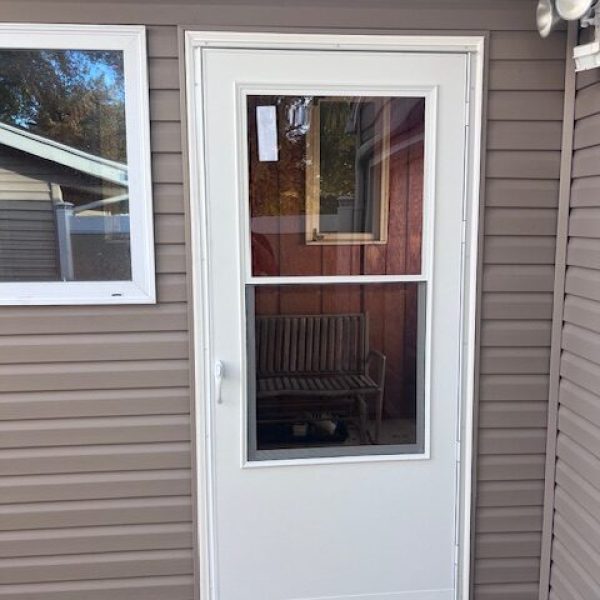 A newly installed white storm door with a large glass panel and a screen, on a house with brown vinyl siding.