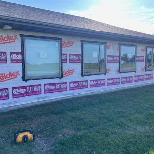 A house under construction with new windows installed and the exterior wrapped in a moisture barrier for insulation and weather protection.
