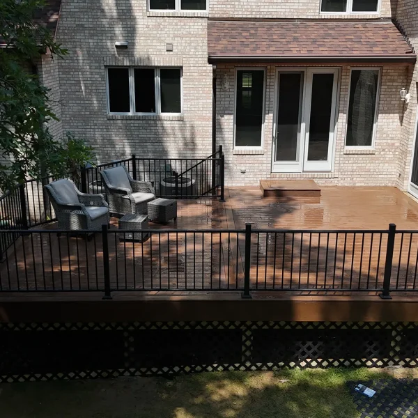 Large residential backyard with a new brown composite deck, black metal railing, and a lattice skirt
